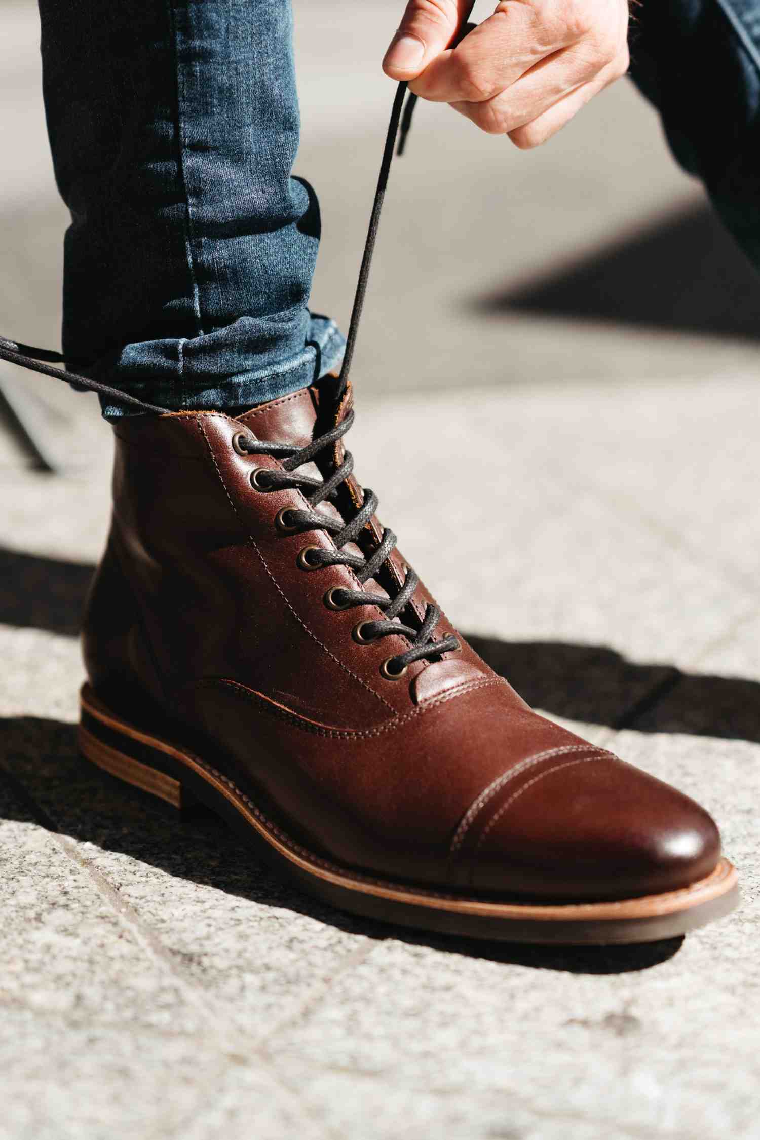 Person lacing up brown leather boot outdoors — Andres Handcrafted Boots