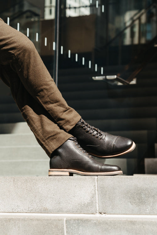 Person wearing brown leather boots and brown pants standing on stone steps.