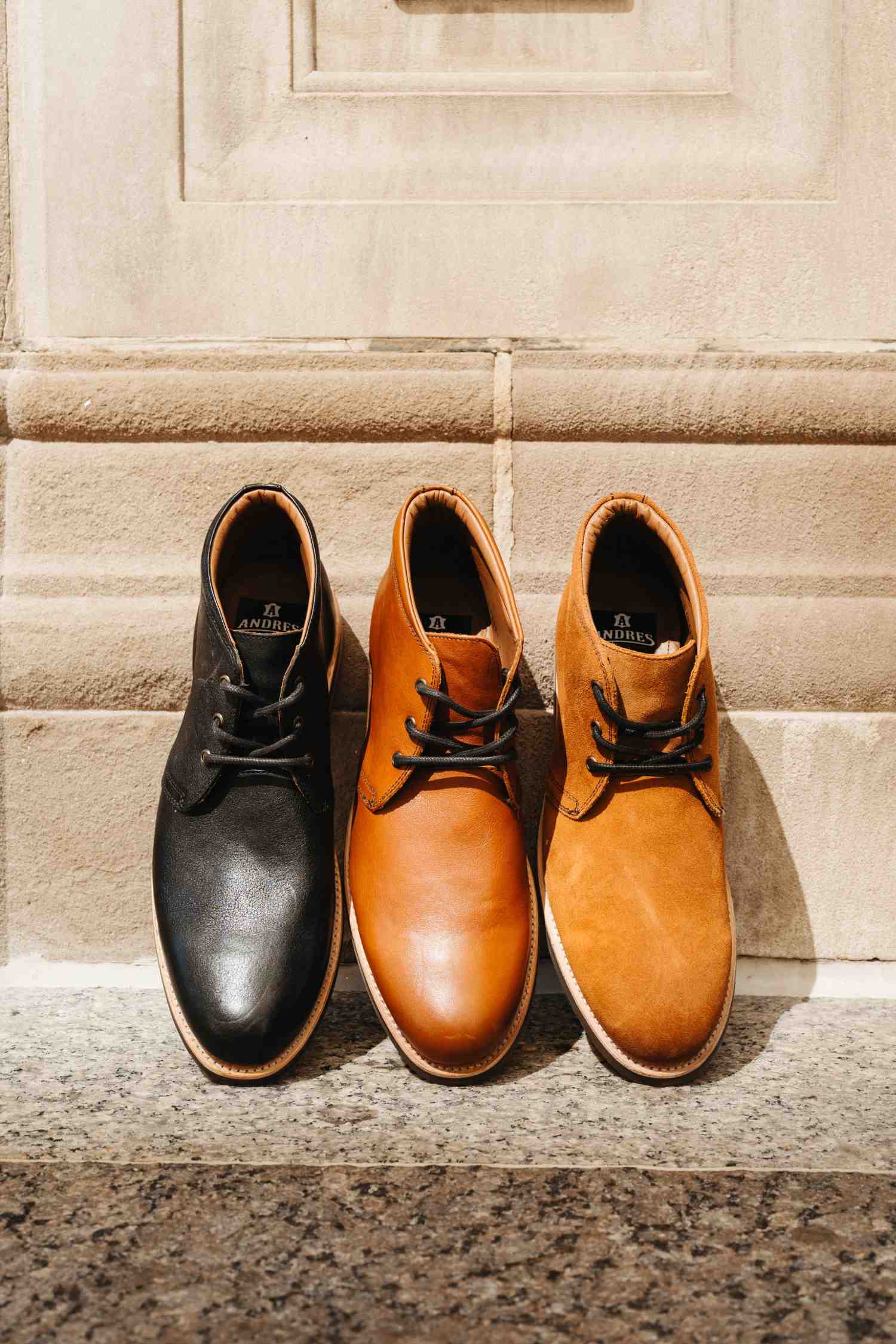 Three Andres Commuter Chukka Boots in black, brown, and tan standing against stone surface — Andres Handcrafted Boots
