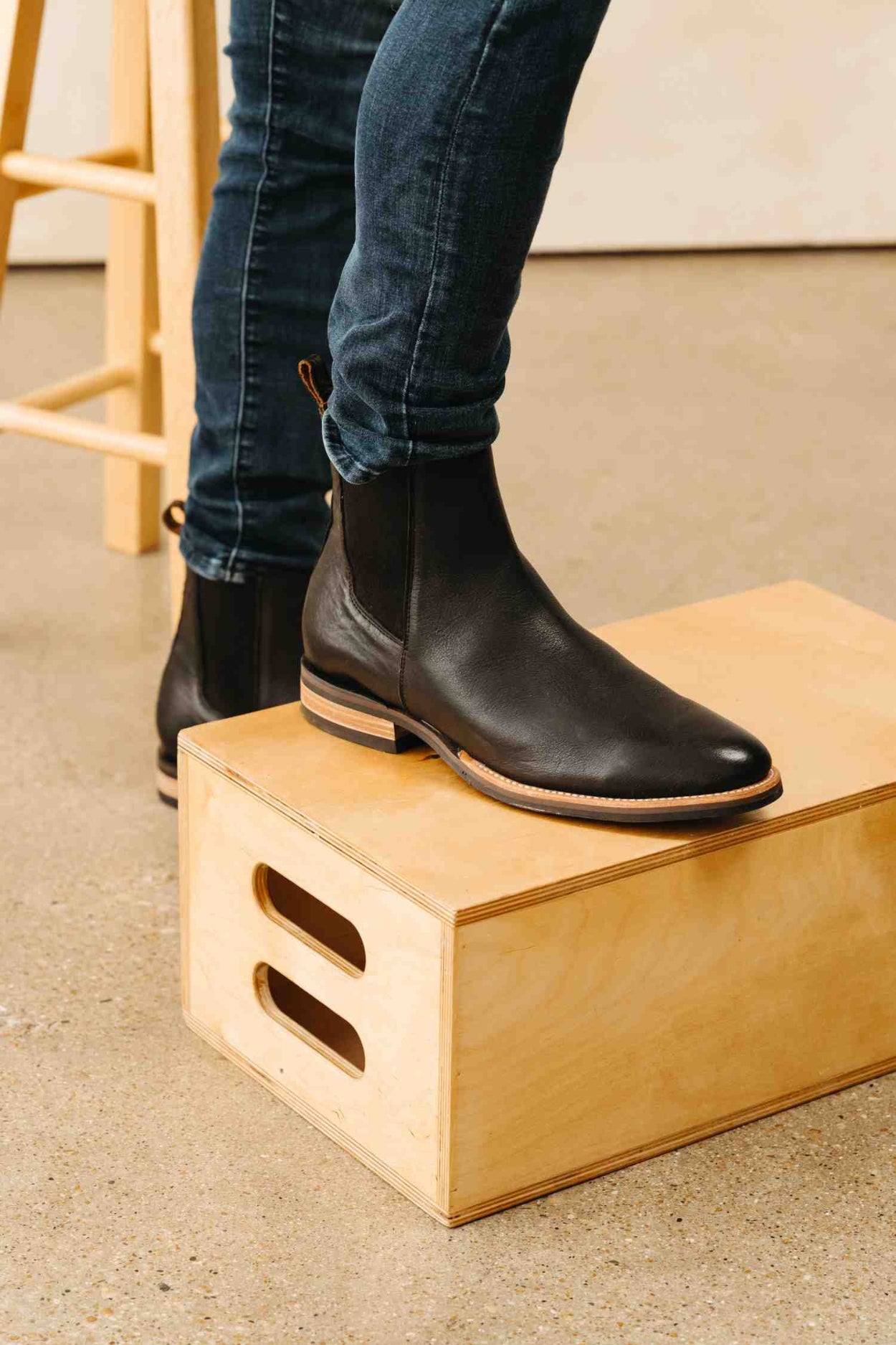 Person wearing black boots stepping onto a wooden block indoors.