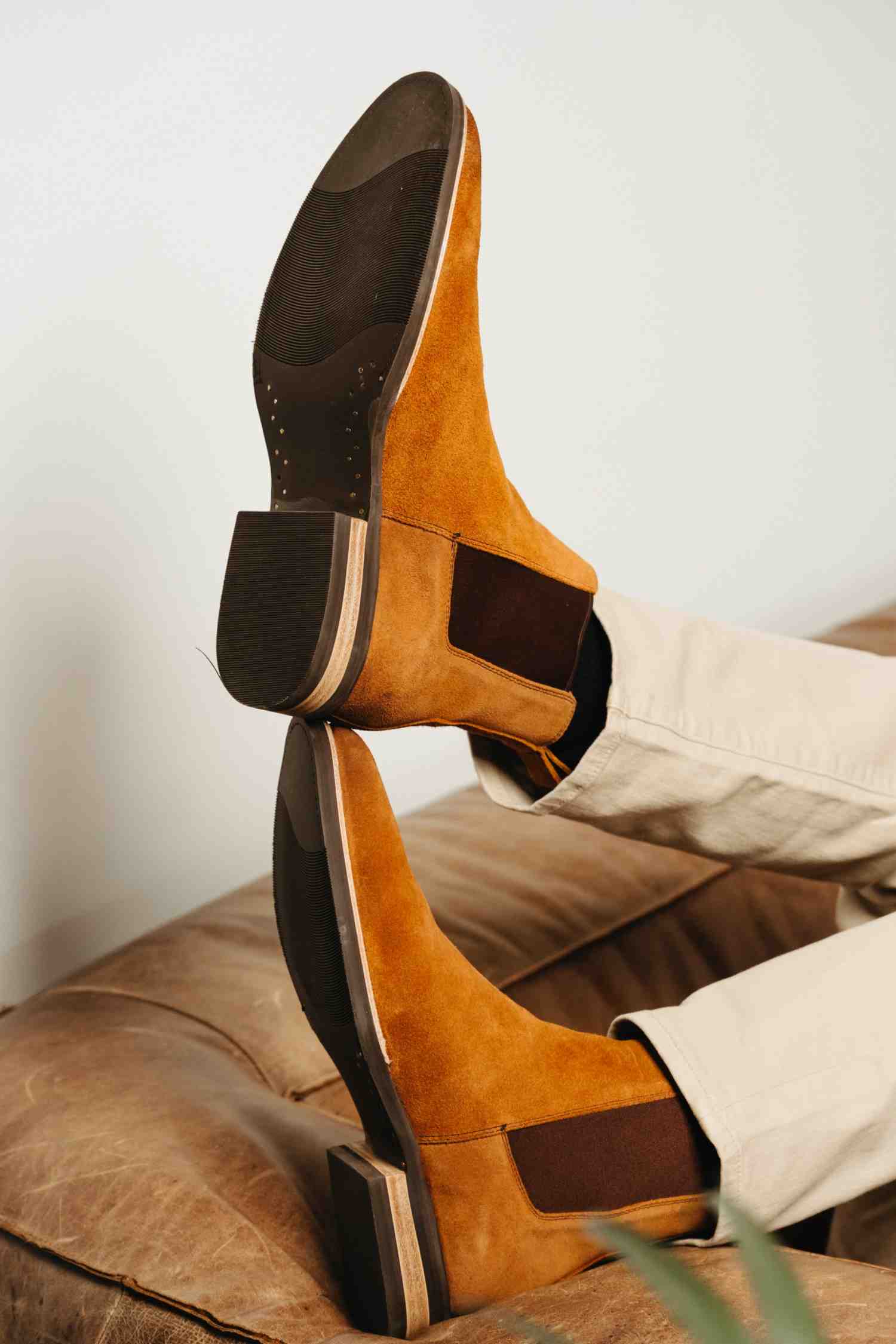 Person wearing tan suede Chelsea boots with feet resting on leather surface — Andres Handcrafted Boots